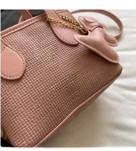Dettaglio borsa a secchiello rosa con trama intrecciata e ciondolo a fiocco e catena oro