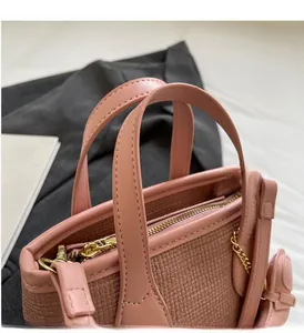 Dettaglio borsa a secchiello rosa intrecciata con manici in pelle e hardware in metallo oro