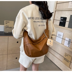 Detail of a brown PU leather dumpling bag with soft plush charm on an adjustable strap