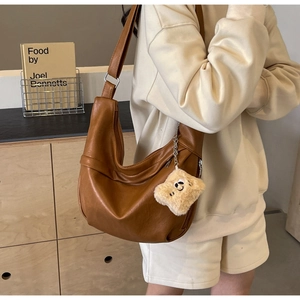 Detailed close-up of brown PU leather hobo bag with a plush smiley charm in a home setting