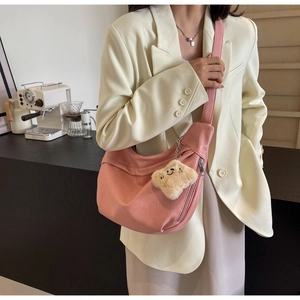 Pink crescent hobo bag with plush charm accessory worn by model in cafe setting