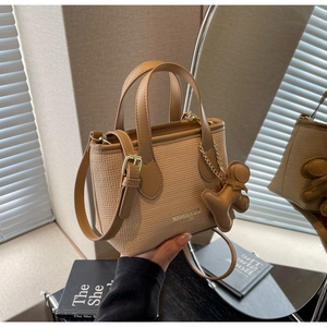 Dettaglio della borsa a secchiello marrone intrecciata con logo dorato e ciondolo a orsetto