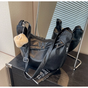 Detail of black crescent shoulder bag with pleated texture and plush charm accessory