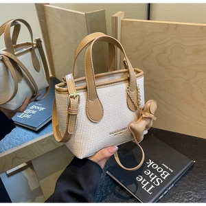 Dettaglio della borsa in tessuto crema con finiture in pelle marrone e ciondolo a orso