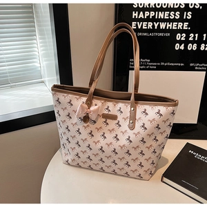 Close-up of beige tote bag featuring horse print, brown leather handles and pink bow detail