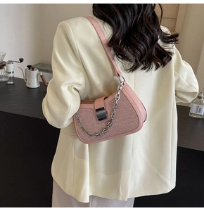 Pink woven underarm bag with silver chain and metal clasp shown on a shoulder