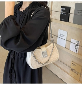 Close-up of beige woven texture bag with silver chain and metal lock on model
