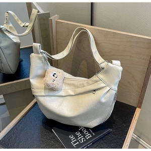Detail of off-white faux leather pleated dumpling bag with plush smiley face pendant