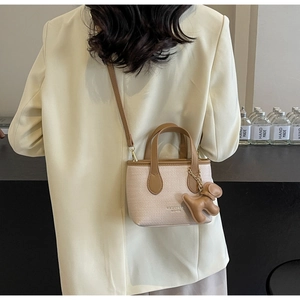 Dettaglio mini borsa a secchiello beige testurizzata con manici in pelle marrone e ciondolo