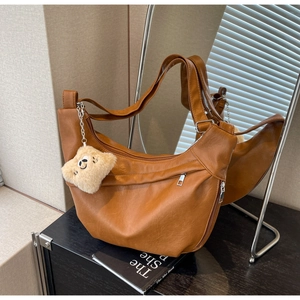 Close-up of brown crescent bag with matte leather texture and cute bear pendant