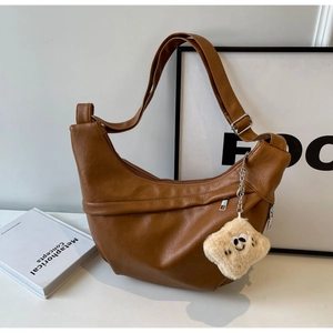 Close-up of brown PU leather crescent bag with pleated details and plush pendant