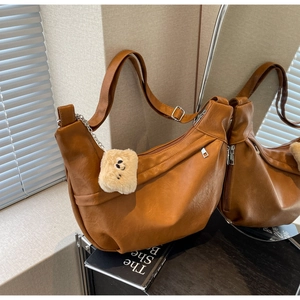 Detail of brown half-moon shoulder bag with adjustable buckle and white plush bear charm