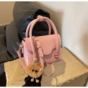 Close-up of pink croc-embossed handbag with gold hardware and a cute plush charm