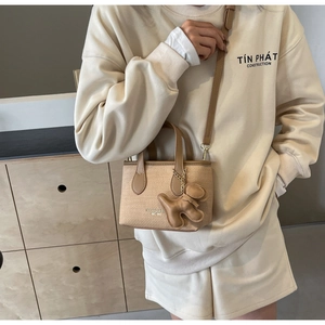 Dettaglio borsa a secchiello beige testurizzata con manici in pelle marrone e ciondolo cane
