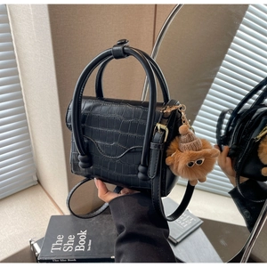 Detail of black crocodile texture handbag with unique plush doll charm and cylindrical handle