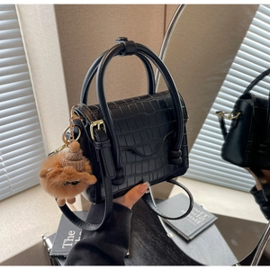 Close-up of black crocodile pattern faux leather bag with gold hardware and plush charm