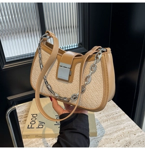 Detailed shot of a beige woven shoulder bag with brown leather trim and silver chain