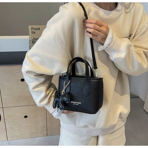 Dettaglio di mini borsa nera intrecciata con ciondolo a cane e logo bianco