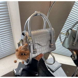 Detail of silver crocodile-embossed mini bag with metallic finish and plush charm