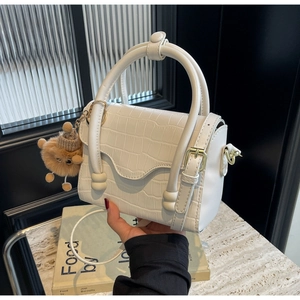 Close-up of white crocodile embossed mini bag with brown pompom charm and top handle