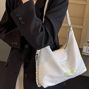 Borsa tote bianca lucida con catena e scritte verdi mostrata sulla spalla del modello