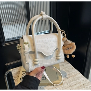 Close-up of white crocodile pattern crossbody bag with round handles and plush pendant