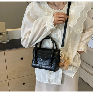 Detail of black crocodile pattern crossbody bag with round handle and plush ball charm