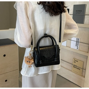 Detailed view of black crocodile pattern crossbody bag with cute plush monster charm