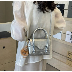Silver crocodile embossed handbag with bear charm shown on model in a minimalist setting