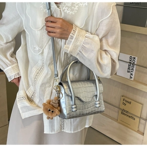 Detailed view of silver crocodile embossed handbag with metal top handles and plush charm
