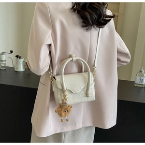 Detail of beige crocodile pattern small crossbody bag with a cute brown plush bear charm