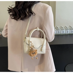 White crocodile pattern crossbody bag with a plush monster charm on a pink suit model