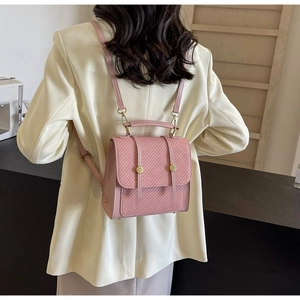 Petit sac à dos rose avec sangles réglables et boucles dorées sur un tailleur beige