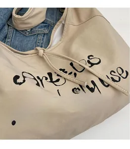 Detail of beige canvas tote bag with black cursive script and reinforced stitching