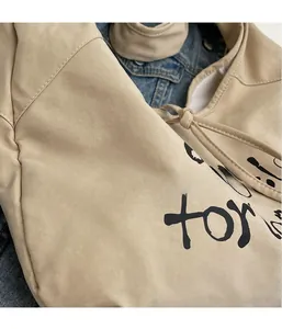 Detail of beige canvas dumpling bag showing soft leather texture and black letter print