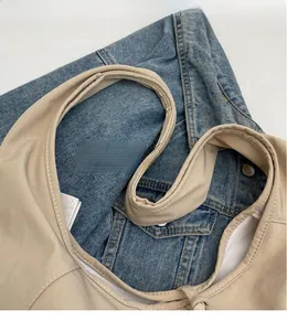 Detail view of smooth wide shoulder strap on a beige canvas hobo bag with denim jacket