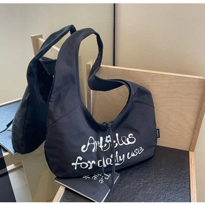 Detail of black canvas hobo bag showing text print and brand tag in minimalist setting