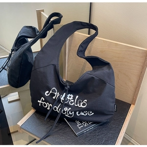 Detail of black canvas hobo bag with white printed text on a wooden stand