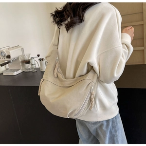 Detail of off-white nylon dumpling bag with woven rope zippers and wide crossbody strap