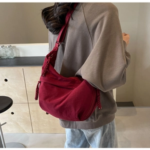 Rear view of a model wearing the large burgundy nylon crescent bag with woven zipper pull