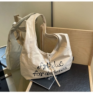 Close-up of cream canvas tote bag with drawstring detail and black text embroidery