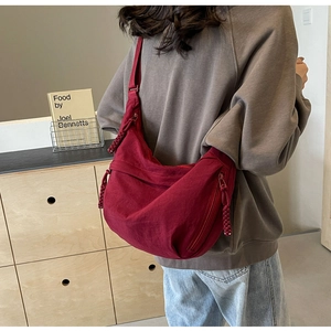 Detail of burgundy nylon crescent bag showing multiple zipper pockets and woven cords