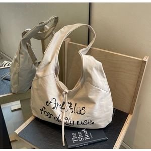 Close-up of cream canvas crescent tote with black script text on a wooden stand