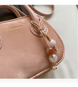 Gros plan d'un sac à main pêche avec logo doré et poignée ornée de perles ethniques