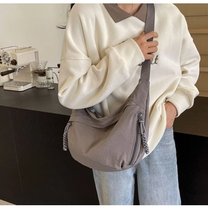 Detailed view of grey nylon crescent bag featuring woven zipper pulls and crossbody strap