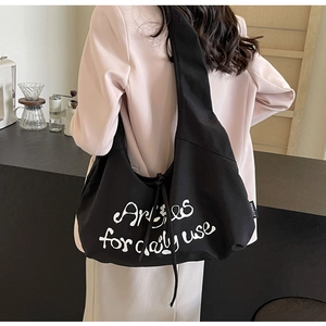 Detailed back view of a large black canvas dumpling bag with white graffiti text and brand tag
