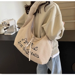 Detail view of beige large-capacity canvas crossbody bag with artistic text on model