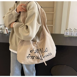 Detail of minimalist beige canvas bag featuring black artistic lettering and wide strap