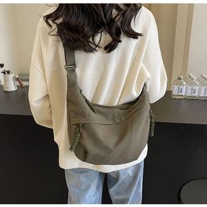 Detail of olive green nylon crossbody bag showing wide strap and woven rope zipper pull