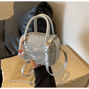 Détail d'un sac à main argenté métallisé avec gland perlé sur fond de pierre